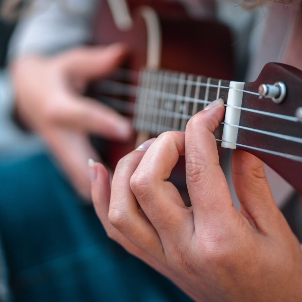 a shallow focus shot of a person wearing jeans while playing a song on the ukulele